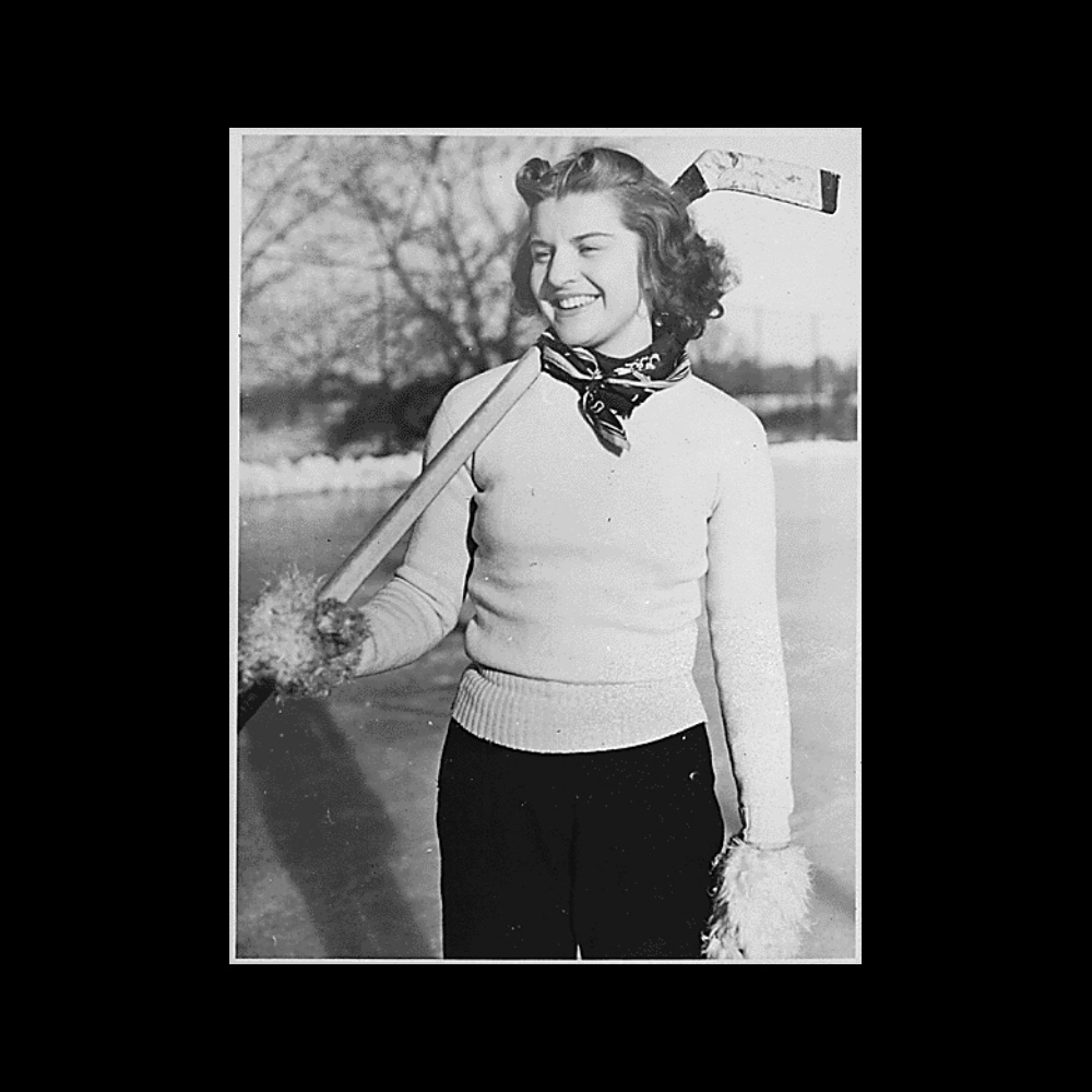Informal photograph of teenage Betty Bloomer, the future First Lady Betty Ford, standing on the ice smiling, while holding a hockey stick over her right shoulder. 1935