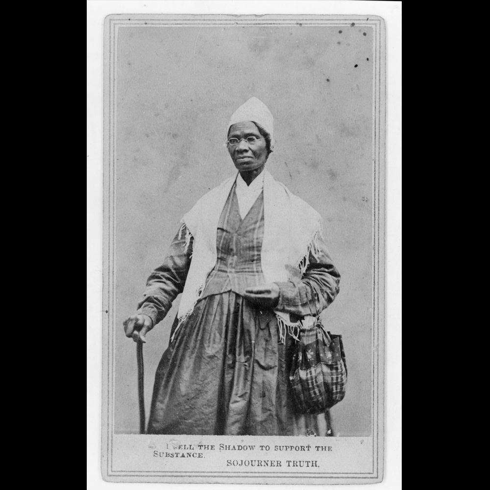 Black and white portrait of abolitionist and Underground Railroad operative Sojourner Truth, standing, wearing spectacles, shawl, and peaked cap, right hand resting on a cane, 1864 ]
