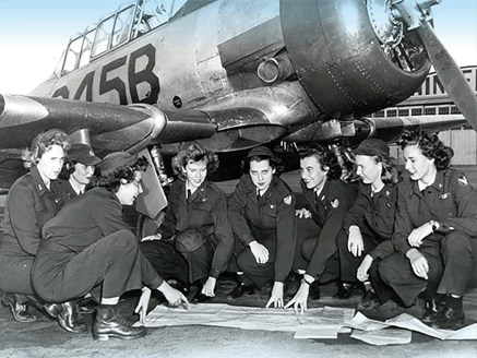 Women Airforce Service Pilots sitting in front of a plan as they look at maps on the floor.